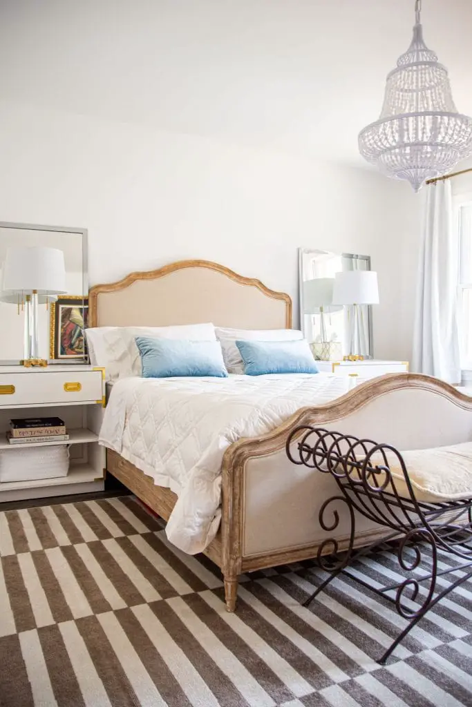 Master bedroom design with french-style upholstered bed, iron bench, and campaign nightstands in white with striped rug by Kevin O'Gara on Thou Swell #bedroom #masterbedroom #bedroomdesign #bedroomdecor #masterbedroomdesign #neutralbedroom #luxurybedroom #interiordesign #homedesign #homedecor